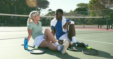 Diverse tennis players resting on court after match, casual outdoor sports break