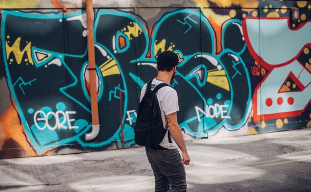 An urban youth exploring colorful street art graffiti mural in the city. This vibrant scene can be used to convey themes of modern lifestyle, urban culture, artistic expression, and exploration. Suitable for content related to art, street culture, youth activities, tourism, and city life.