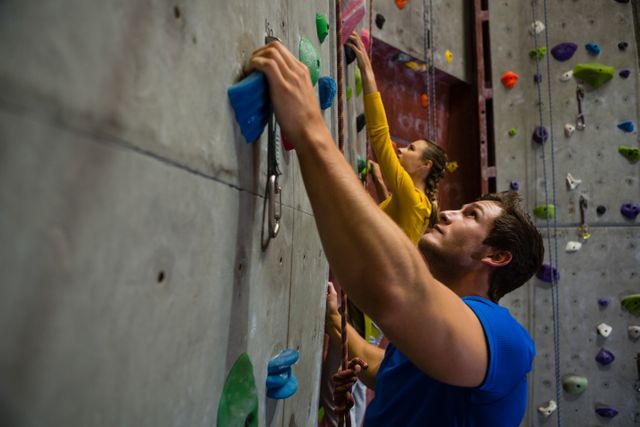 Two athletes are climbing an indoor rock wall, showcasing teamwork and determination. Ideal for promoting fitness, health clubs, and active lifestyles. Can be used in advertisements for gyms, sports equipment, and motivational content.
