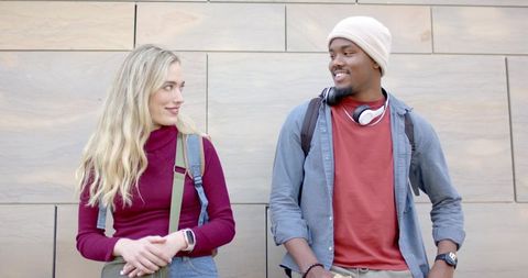 Diverse college students chatting on campus wearing backpacks and headphones beside tile wall