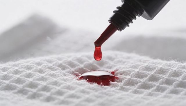 Macro red drop forming crimson stain on white waffle fabric with black applicator nozzle