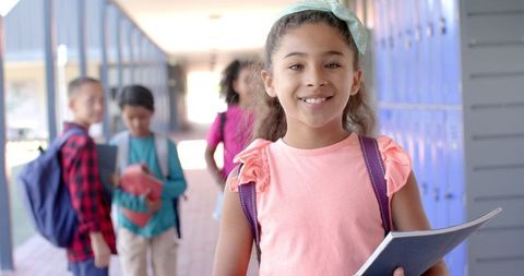 Confident Girl Holding Book in School Hallway with Diverse Peers - Download Free Stock Images Pikwizard.com