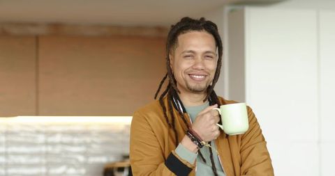 Smiling african american man holding mug in modern kitchen, casual morning coffee moment