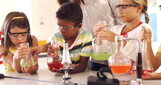 Group of young students conducting chemistry experiments at school. They are wearing protective goggles and examining their colorful chemical mixtures in flasks. Perfect for educational materials, science outreach programs, and advertising STEM initiatives aimed at children.