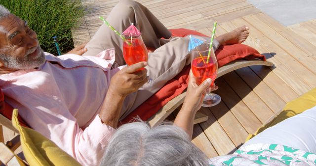Senior couple relaxing on sun loungers outdoors, enjoying tropical cocktails. Ideal for concepts of retirement, leisure, relaxation, and vacations. Suitable for advertisements in tourism, lifestyle articles, and wellness programs targeting older adults.