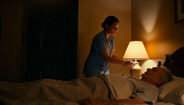 Night homecare nurse adjusting lamp while tending elderly patient in bed