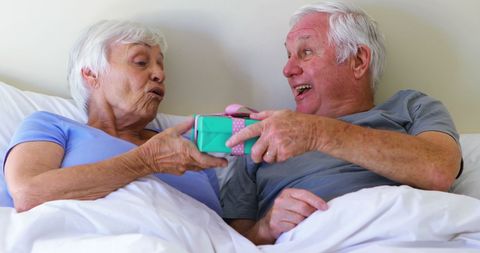 Joyful Senior Couple Sharing Surprise Gift in Bedroom