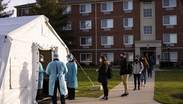College students queuing for outdoor covid testing tent on campus lawn at sunrise