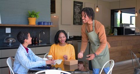 Cozy modern cafe scene with African American barista serving takeaway box to two women