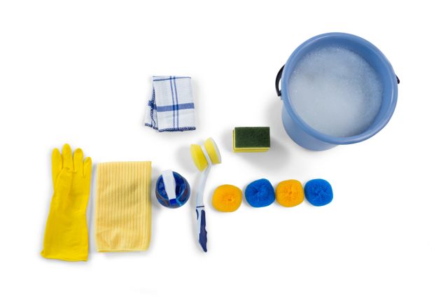 Overhead view of various cleaning supplies including a bucket with soapy water, yellow gloves, sponges, a brush, and cleaning cloths. Ideal for use in articles, advertisements, or instructional materials related to household cleaning, hygiene, and maintenance.