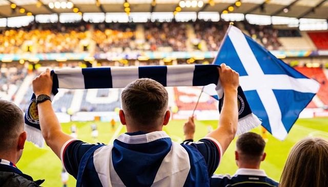 Scottish football fans cheering and waving saltire flag with navy white scarves at stadium