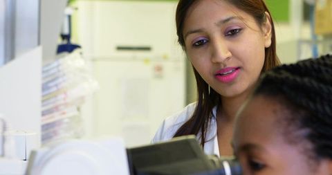 Indian scientist mentoring trainee at compound microscope, lab research and diagnostics