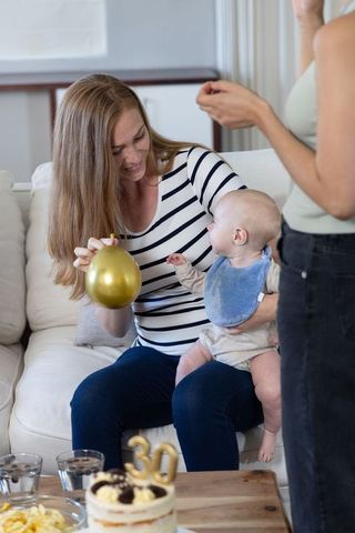 Mother with infant celebrating birthday at home with cake and balloon