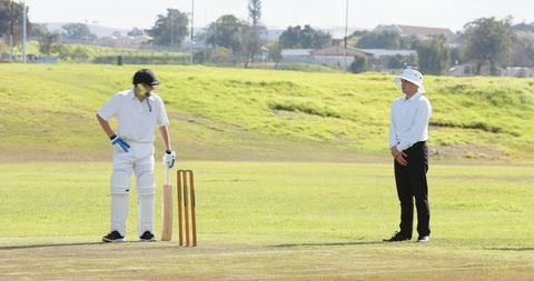 Batsman and umpire on sunny outdoor cricket pitch