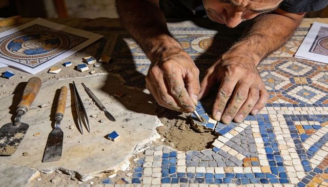 Artisan restoring antique mosaic, placing blue tesserae into mortar with tweezers