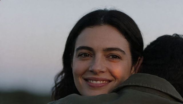 Smiling woman hugging partner at dusk with warm sunset glow and olive green jacket