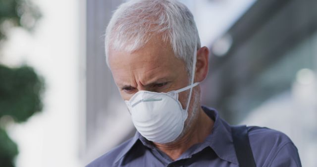 Senior man with gray hair and medical mask focused outdoors. Perfect for themes related to public health, protection against coronavirus, and safety measures for the elderly. Useful for articles on healthcare, social distancing, and pandemics.
