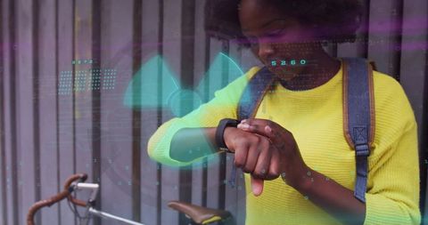 Woman checking smartwatch while wearing yellow sweater and backpack beside city bicycle