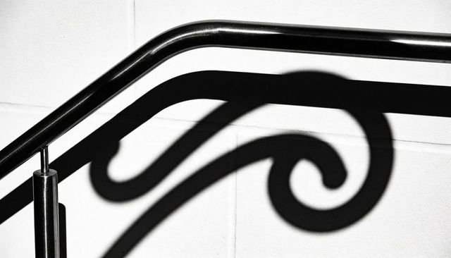 Curved stainless handrail casting dramatic scroll shadow on white tiled wall minimal design