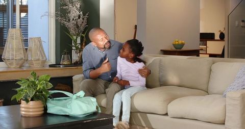Mature african american father talking and hugging daughter on beige sofa in cozy living room