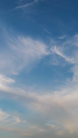 Vertical time-lapse curling cirrus clouds at sunset with contrail and soft sky gradient