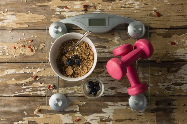 Overhead view of bowl of breakfast and dumbbells on weighing scale