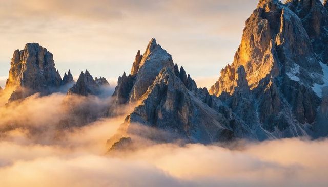 Golden sunrise on jagged alpine peaks emerging through low mist and pastel clouds