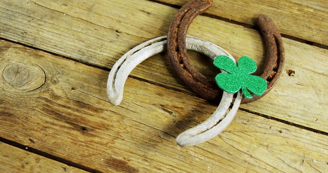 A pair of old horseshoes and a green, glittery shamrock rest on a rustic wooden surface, symbolizing luck and the celebration of St. Patrick's Day. These items evoke a sense of tradition and folklore associated with Irish culture.