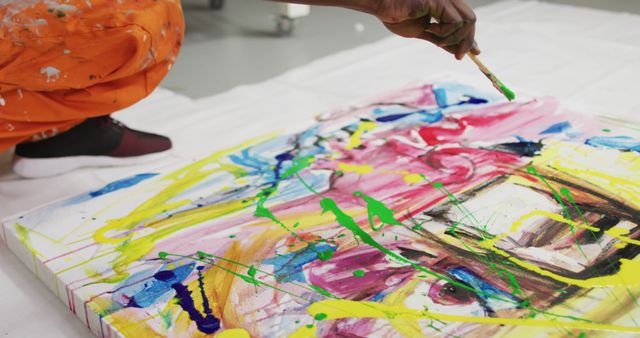 Close up of african american male artist pouring paint with a paint brush on canvas at art studio. art, hobby and creative occupation concept