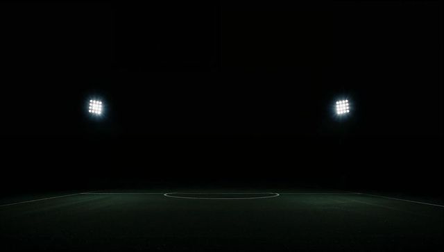 Empty sports pitch glowing center circle under twin floodlights at night