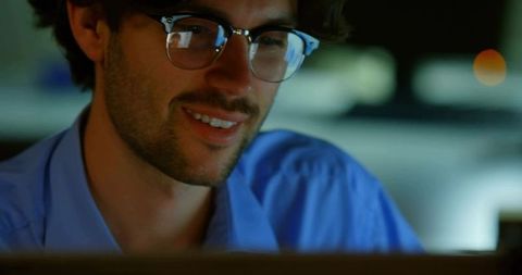 Smiling Man Using Laptop with Clear-Framed Glasses in Home Office