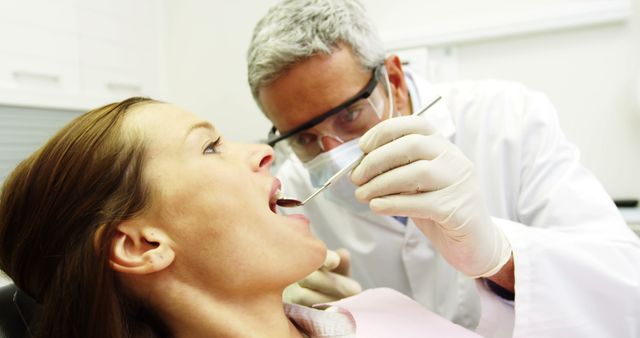 Dentist examining female patient's teeth, maintaining oral health. Useful for articles on dentistry, professional healthcare settings, dental clinics, dental education and oral hygiene tips. This image is suitable for websites on dental services, medical blogs, dentist advertisements, and dental care brochures.