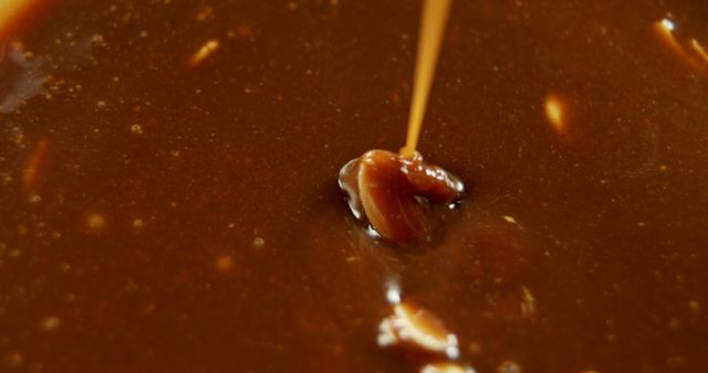 Warm caramel sauce pouring into a golden brown mixture, suitable for cooking, dessert preparation, baking blogs, or food-themed projects focusing on rich and indulgent treats.