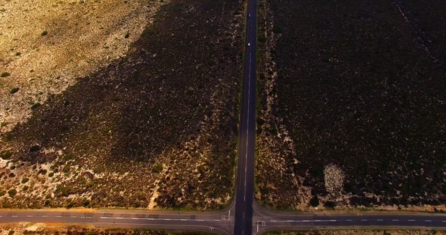 Aerial view of a desert road intersection illuminated by the warm light of the setting sun, creating beautiful contrasts with the dark asphalt and surrounding arid landscape. This image is perfect for travel blogs, articles on road trips, and websites related to transportation infrastructure. It can also be used in environmental studies, geographic resources, and advertisements promoting off-road adventures.