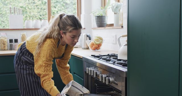 A woman with blonde hair and casual apparel, preparing to bake by placing a tray into the oven. Ideal for content related to home cooking, lifestyle, baking tutorials, kitchen appliances, and domestic routines.