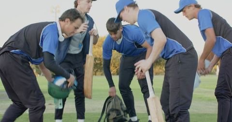 Teenage cricket team gathering gear on field preparing for match and batting practice