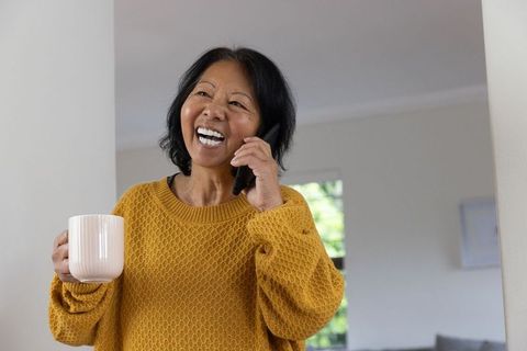 Senior Woman Cheerfully Talking on Smartphone with a Cup of Coffee at Home