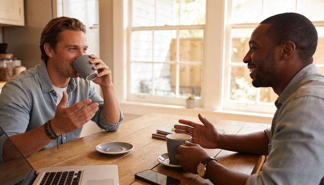 Sunlit kitchen conversation between two friends sharing coffee, laughing, and discussing ideas