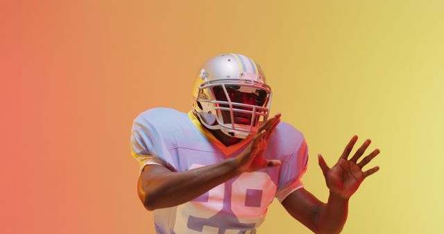 Depicts a professional American football player dressed in full protective gear, captured in an intense action pose against a multicolor gradient background. Use this image for promoting sports events, team sports articles, athletic wear advertisements, or dynamic lifestyle content.