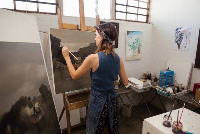 Young woman painting on a canvas in an art studio, focusing on her work. Ideal for use in articles or advertisements related to art classes, creative hobbies, artistic inspiration, or educational programs in fine arts. Can also be used to depict the concept of concentration and dedication in creative pursuits.