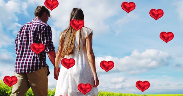 Composite of red heart balloon icons over caucasian couple holding hands in field. Love, romance and valentine's day concept digitally generated image.