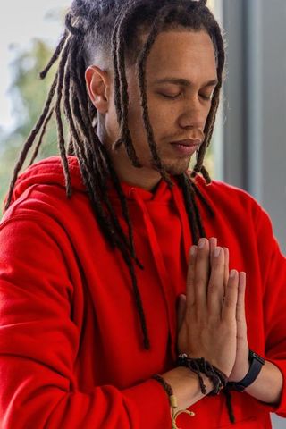 African american man meditating with pressed hands wearing red hoodie and dreadlocks