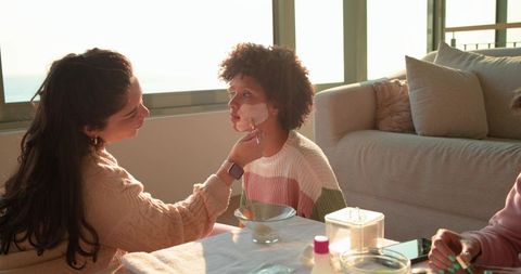 Diverse women applying face mask together during cozy home spa afternoon