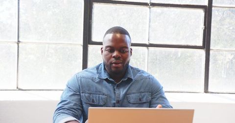 Businessman in Denim Shirt Focused on Laptop in Bright Office