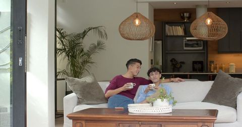 Happy Asian Couple Relaxing with Coffee on Modern Living Room Sofa