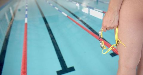 Person holding goggles by calm swimming pool lane lines