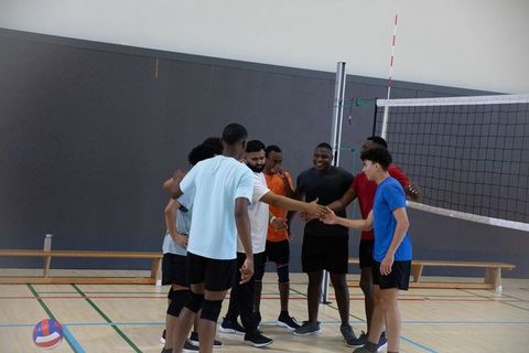 Multiracial men shaking hands at volleyball net in gym showing teamwork and sportsmanship