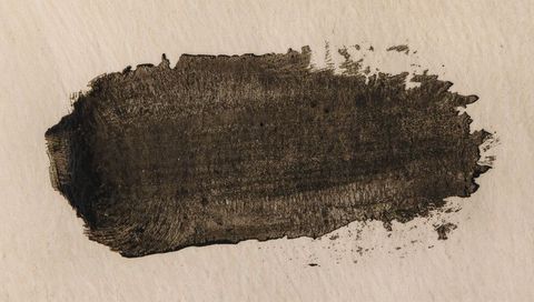 Wide dark ink brushstroke on cream paper with bristle marks, splatters and paper grain texture