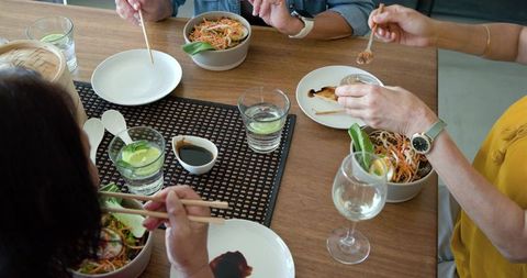 Diverse women sharing noodle salads and dipping chopsticks into soy sauce