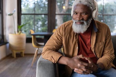 Senior african american man listening with headphones wearing smartwatch relaxing on sofa